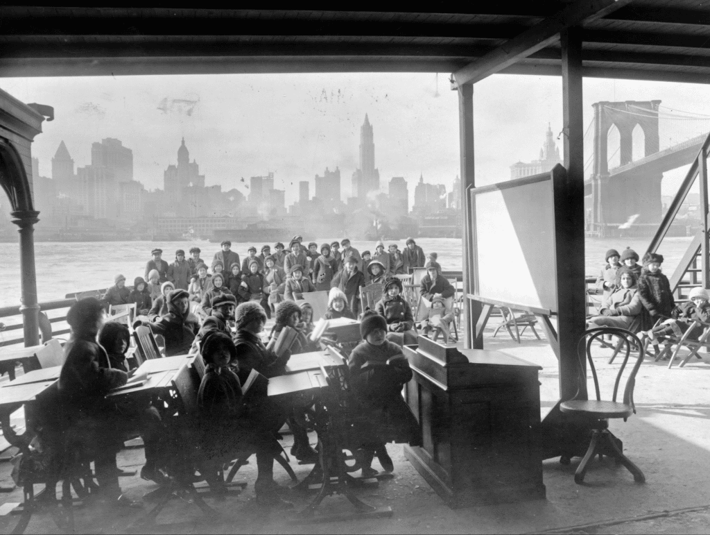 Black and white photo of children attending class on a ferry in New York City, 1915.