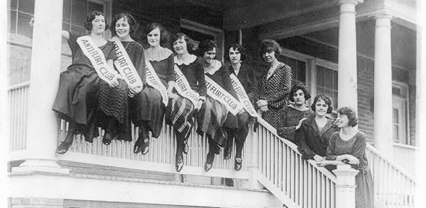 10 women sitting and standing on the porch of the Anti-Flirt Club House. 