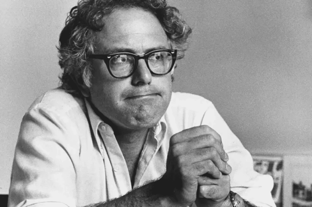 Young Bernie Sanders sitting with hands clasped with disappointed expression.